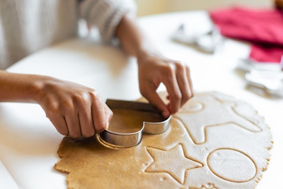 Close-up of a child's hands making gingerbread cookies using cookie cutters. 