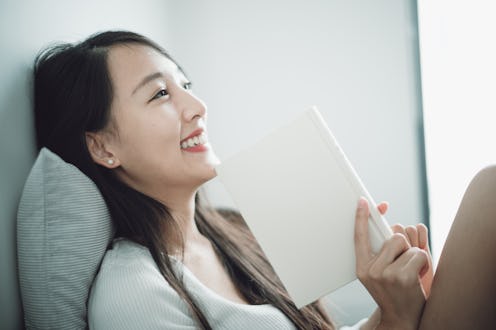 Beautiful Asian young woman relaxing at home and reading novel.