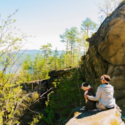 person with dog sitting on a rock in the mountains