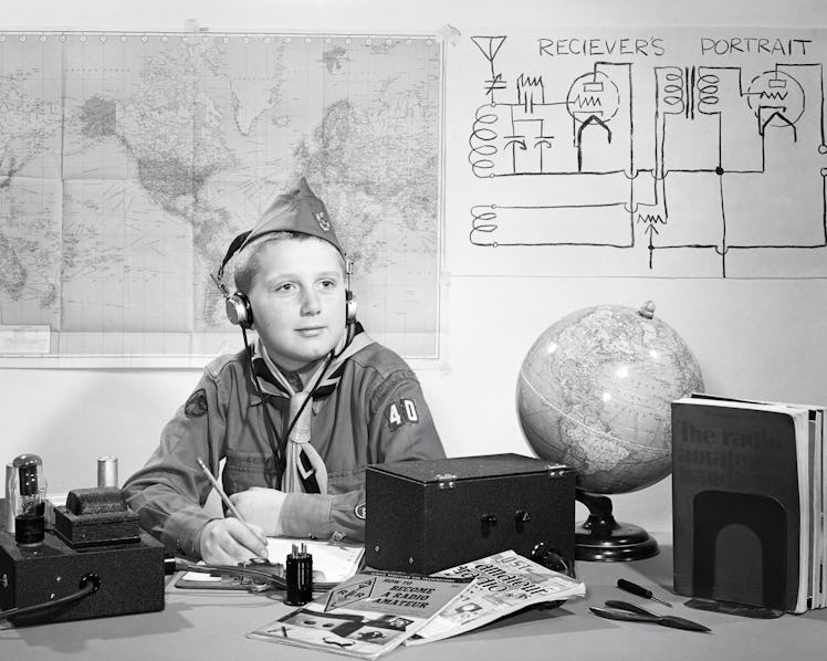 1950s boy scout in uniform a amateur ham radio operator sitting at desk wearing earphones listening ...