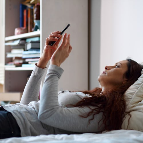 Woman in bed holding a smart phone. The only connection to the world.