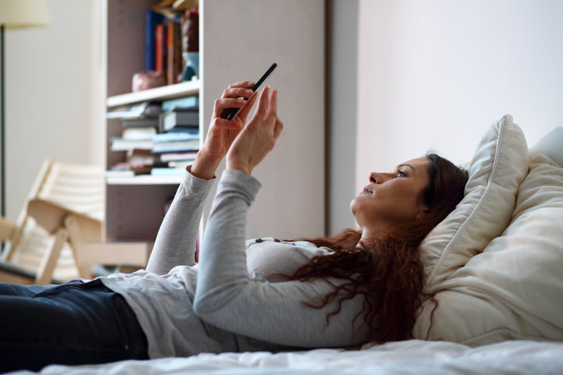 Woman in bed holding a smart phone. The only connection to the world.