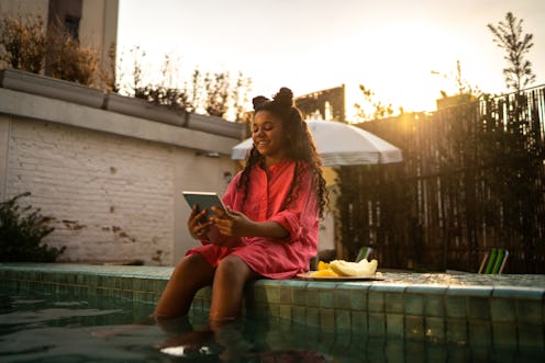 Girl sitting by the pool using digital tablet at home