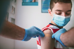 Image of a teenager getting a bandage placed on the upper shoulder by a gloved doctor.