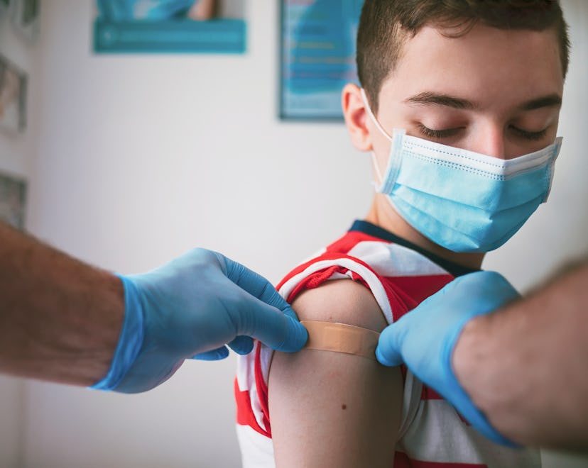 Image of a teenager getting a bandage placed on the upper shoulder by a gloved doctor.