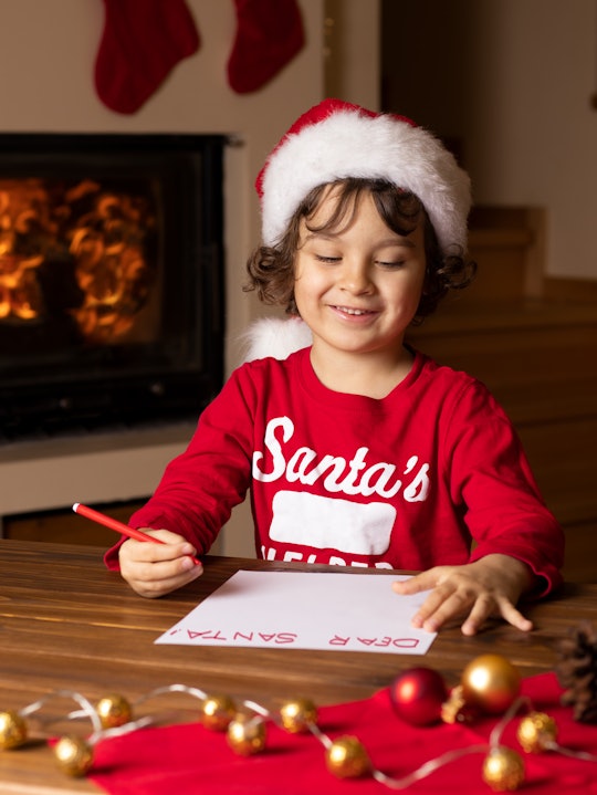 Photo of 5- year child in Santa hat writing letter to Santa. Fireplace, Christmas decorations