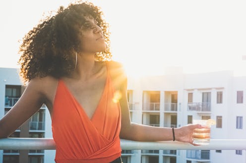Beautiful young woman on a rooftop in a city with warm sunflare and a drink in hand
