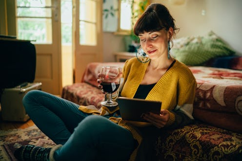 Young woman at home drinking red wine and using tablet