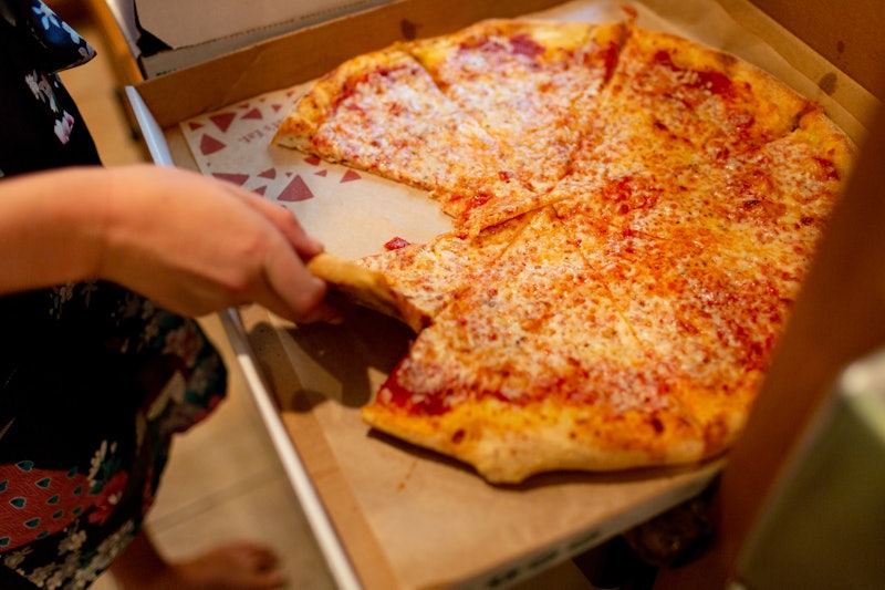 Cheese pizza in box with woman getting a slice