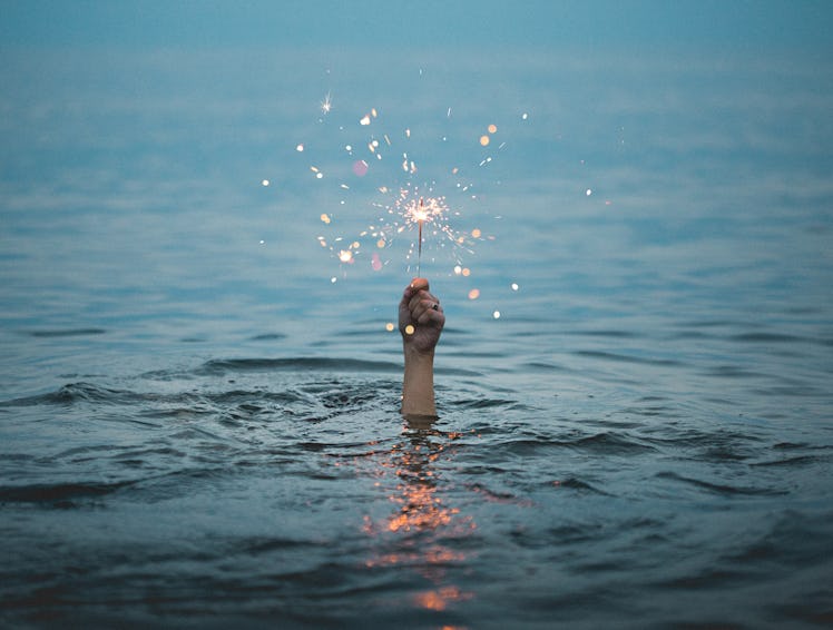 Young woman submerged in the ocean, holding a sparkler above the water, thinking about how her zodia...