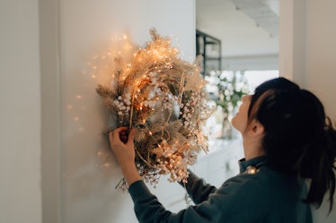 Photo of a young woman decorating the living room of her apartment with some solstice decorations.