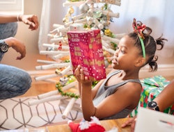 Excited little girl sitting with her family about to open a gift on Christmas morning