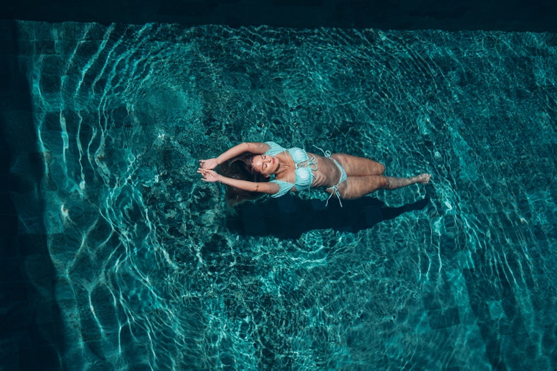Attractive young woman is floating on water in the pool.