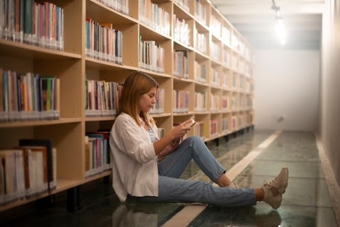 portrait of girl reading book leaning on shelves in city library