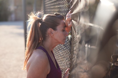 An exhausted woman from running is resting her head in a wired fence.