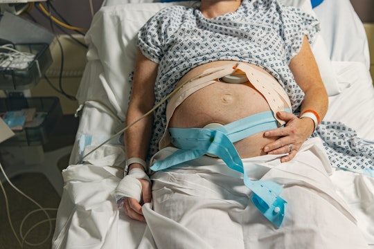 An unrecognisable mature pregnant woman lies on a hospital delivery bed as she has fetal monitoring....