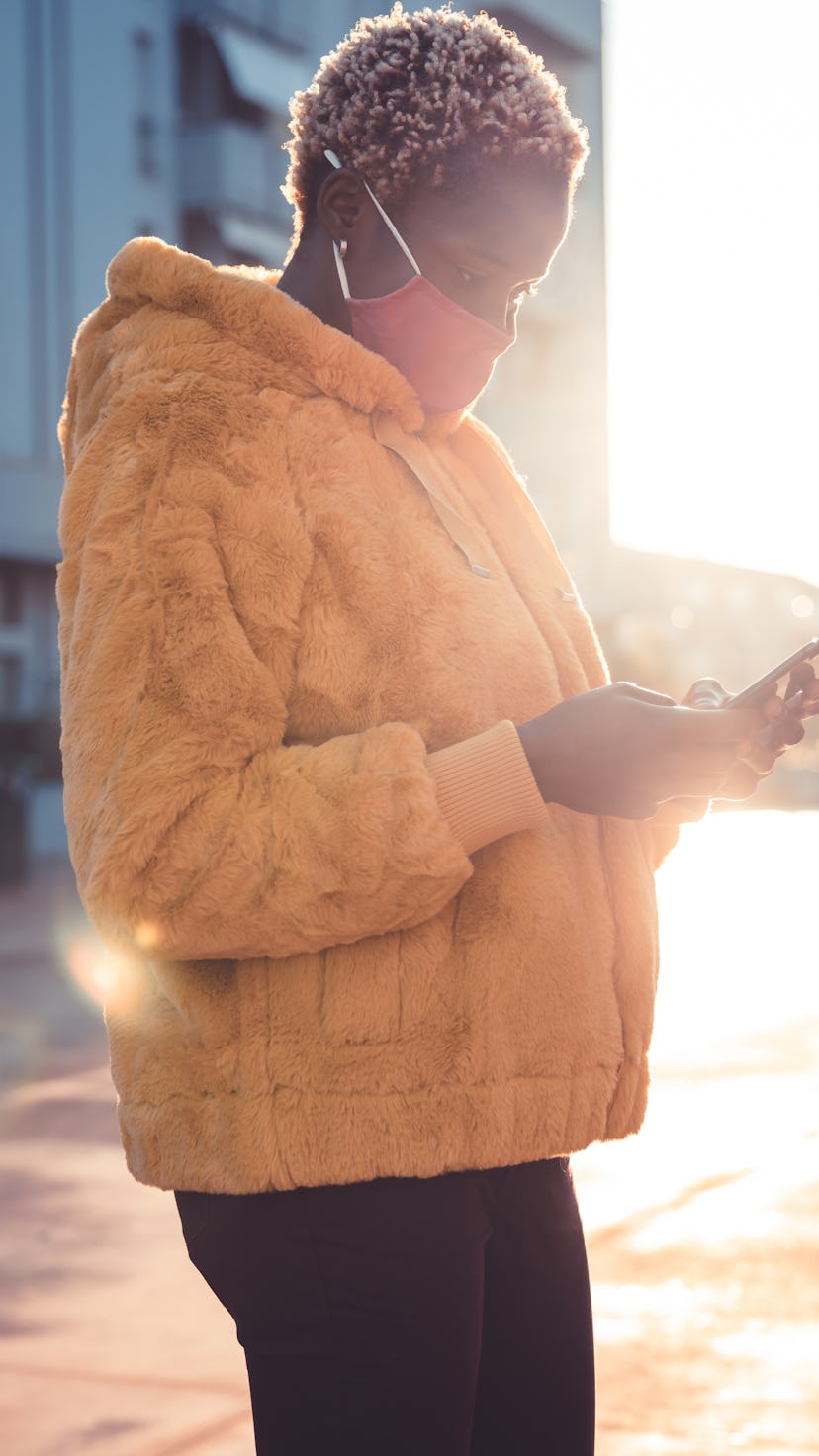 Young woman walking in the neighborhood wearing a yellow coat with a pink cloth mask.