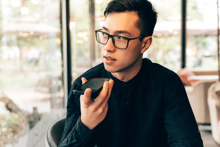 Smart and handsome Asian entrepreneur in glasses is using mobile phone to record an audio message or...