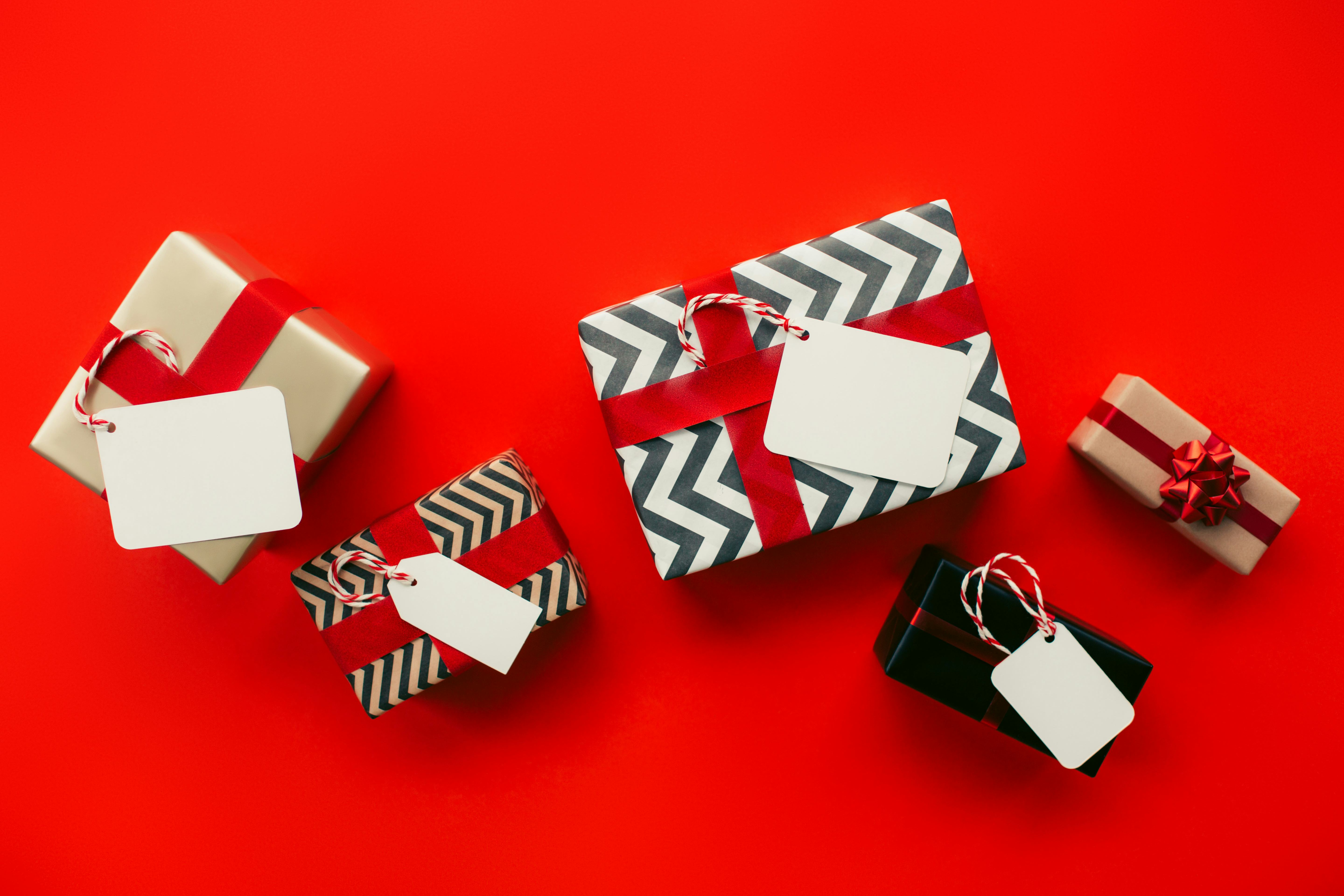 Top view of bunch of gift boxes with empty labels and paper wrapping placed on red background during...