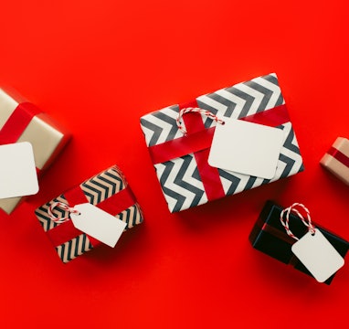 Top view of bunch of gift boxes with empty labels and paper wrapping placed on red background during...