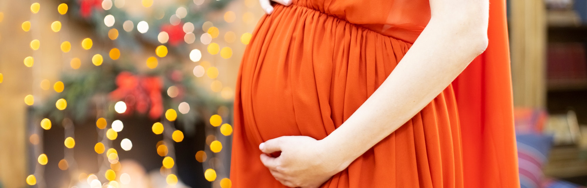 best christmas gift. faceless pregnant woman in a red dress hugs her belly against the background of...