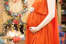 best christmas gift. faceless pregnant woman in a red dress hugs her belly against the background of...