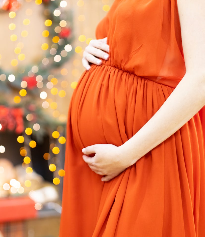 best christmas gift. faceless pregnant woman in a red dress hugs her belly against the background of...