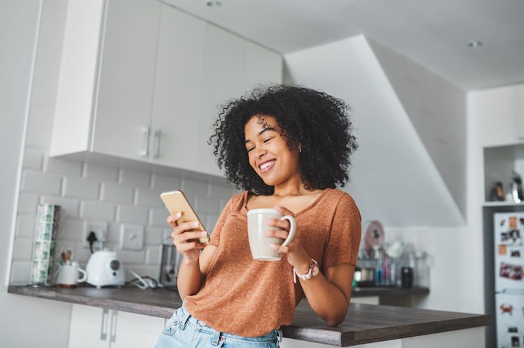 Shot of a young woman using a smartphone and having tea in the kitchen at home, for which she'll nee...