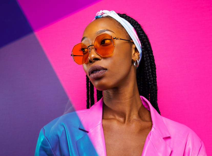 Young woman wearing sunglasses in front of a pink background, thinking about the spiritual meaning o...