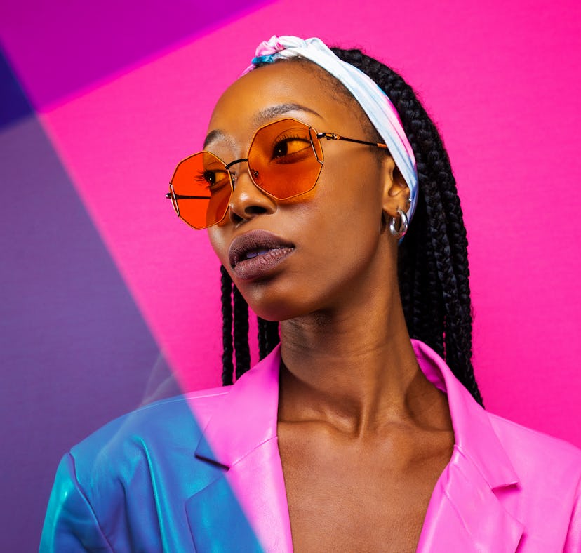 Young woman wearing sunglasses in front of a pink background, thinking about the spiritual meaning o...