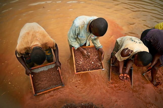 Miners sifting through the selected rich rock fragments in search of a diamond gem near an Angolan v...