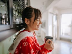 Portrait of a young woman drinking hot chocolate in the kitchen of her apartment; enjoying the lovel...