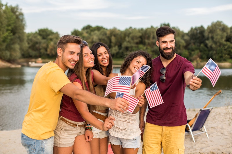 Three quarter length shot of five cheerful friends waving American flags and smiling while celebrati...
