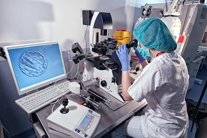Embryologist girl looking through a microscope and adding sperm to egg in laboratory of reproductive...