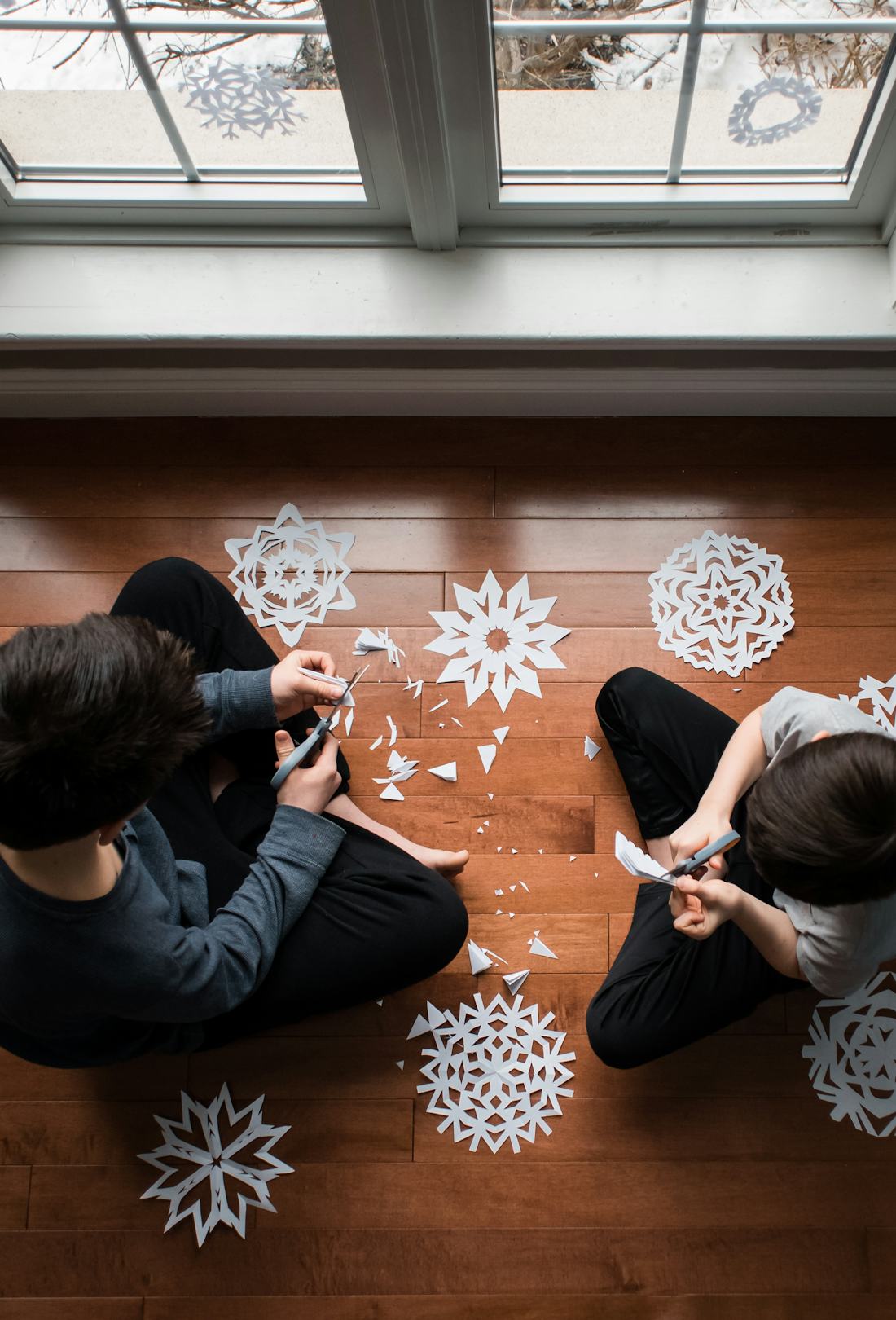 Two kids sitting on the floor making snow crafts - paper snowflakes