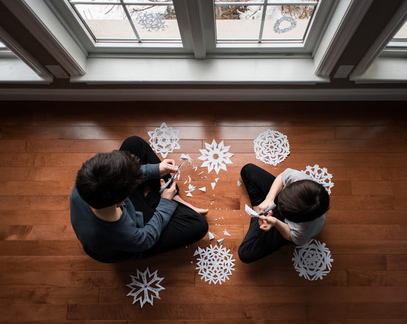Two kids sitting on the floor making snow crafts - paper snowflakes