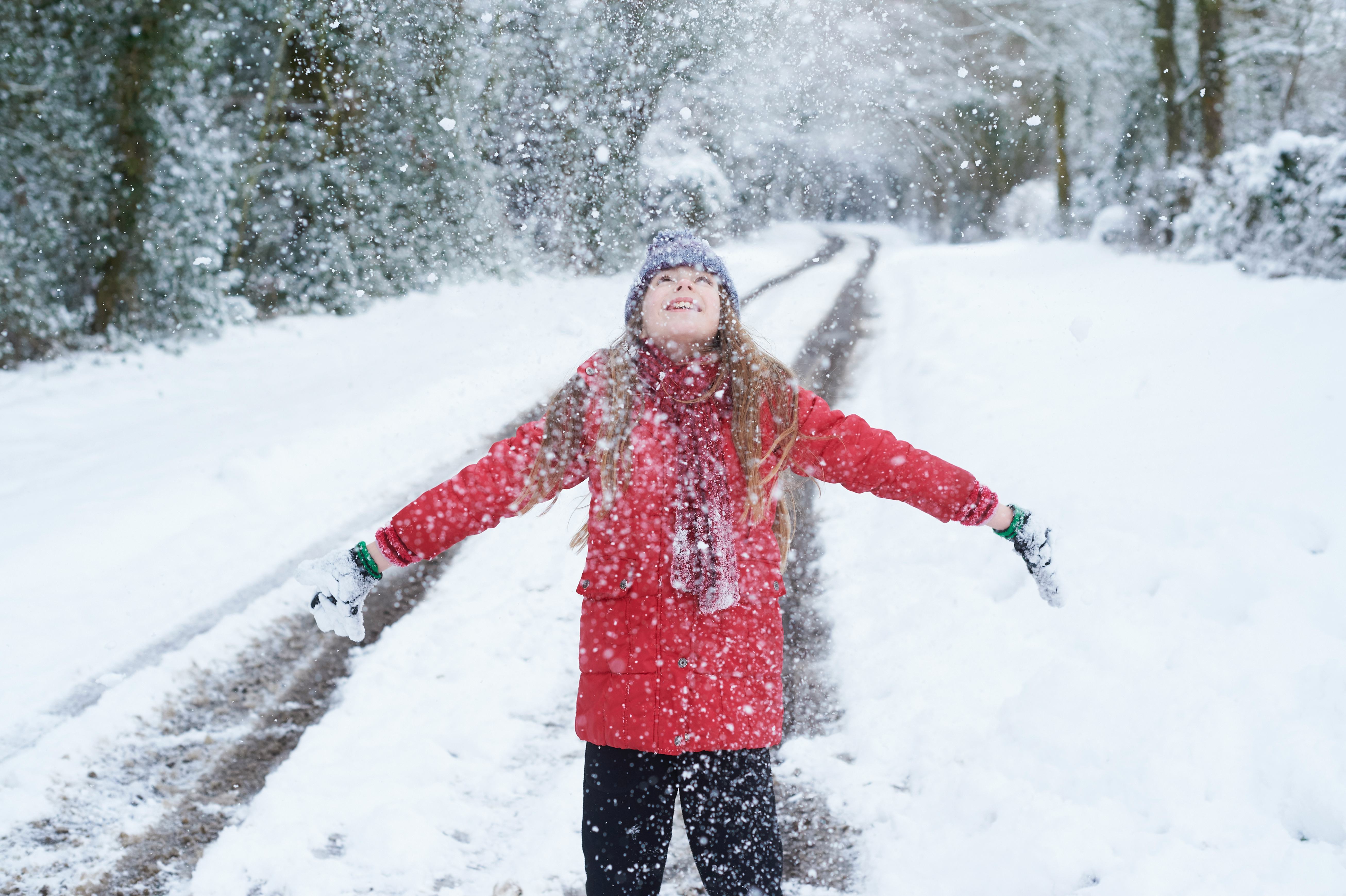 A girl in a red jacket looking up at snow falling with arms wide open