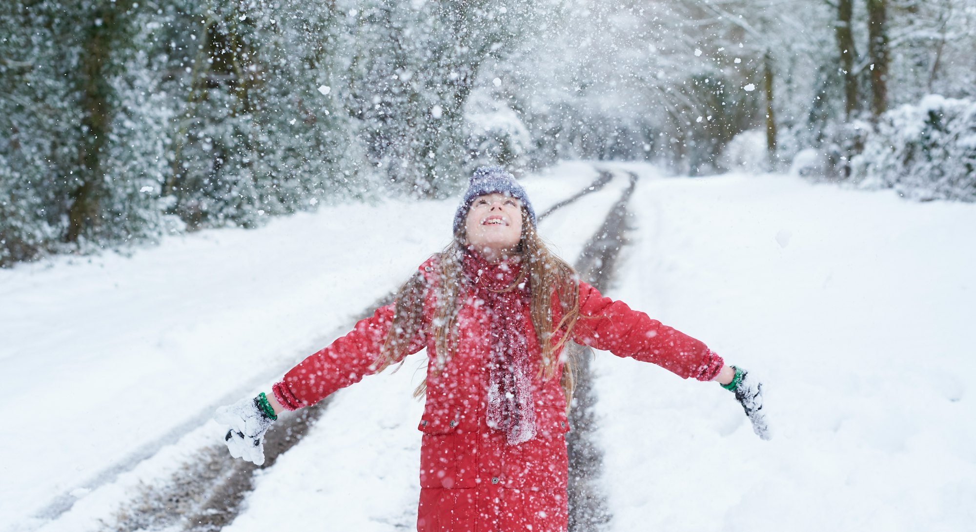 A girl in a red jacket looking up at snow falling with arms wide open