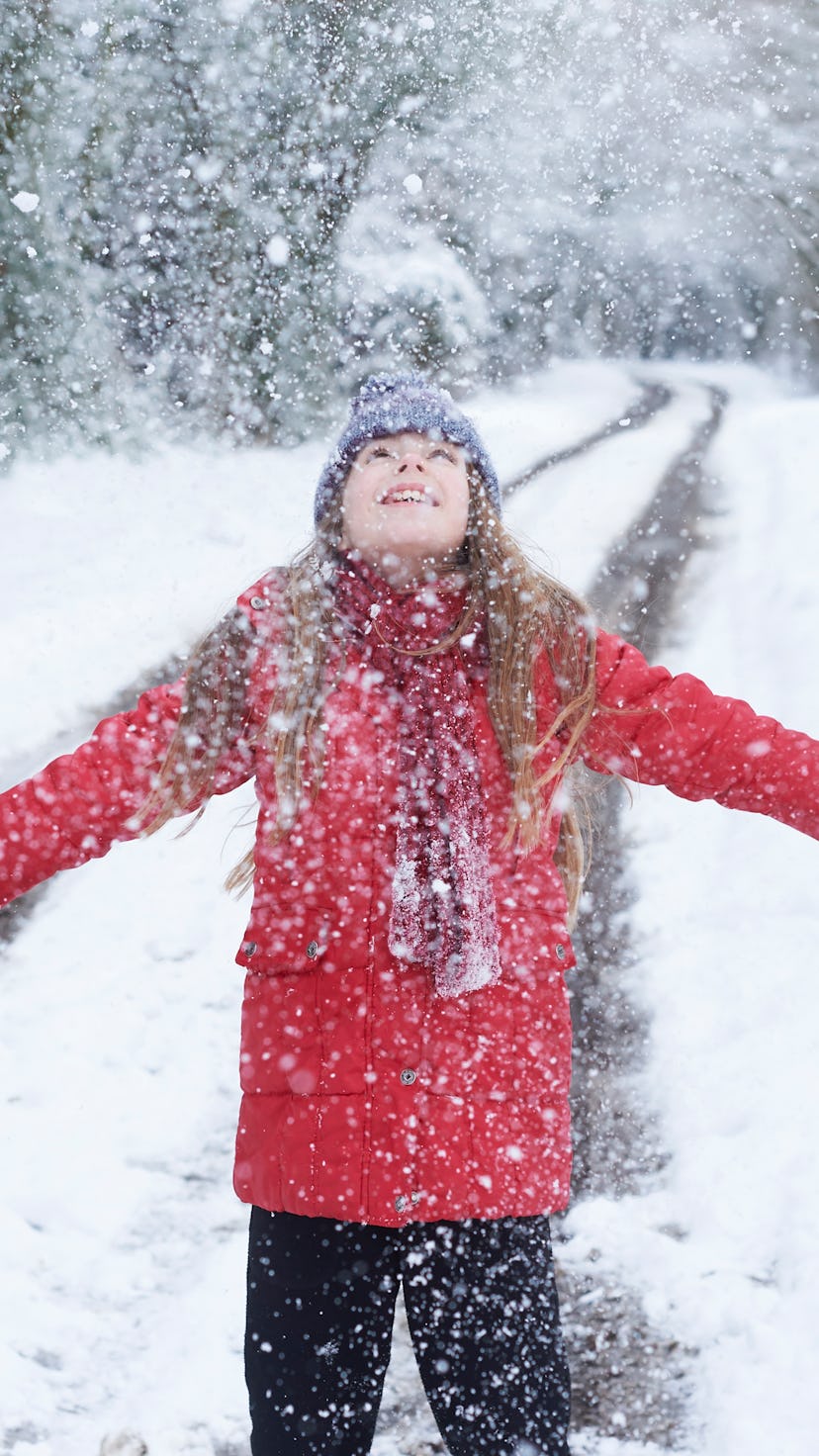 A girl in a red jacket looking up at snow falling with arms wide open