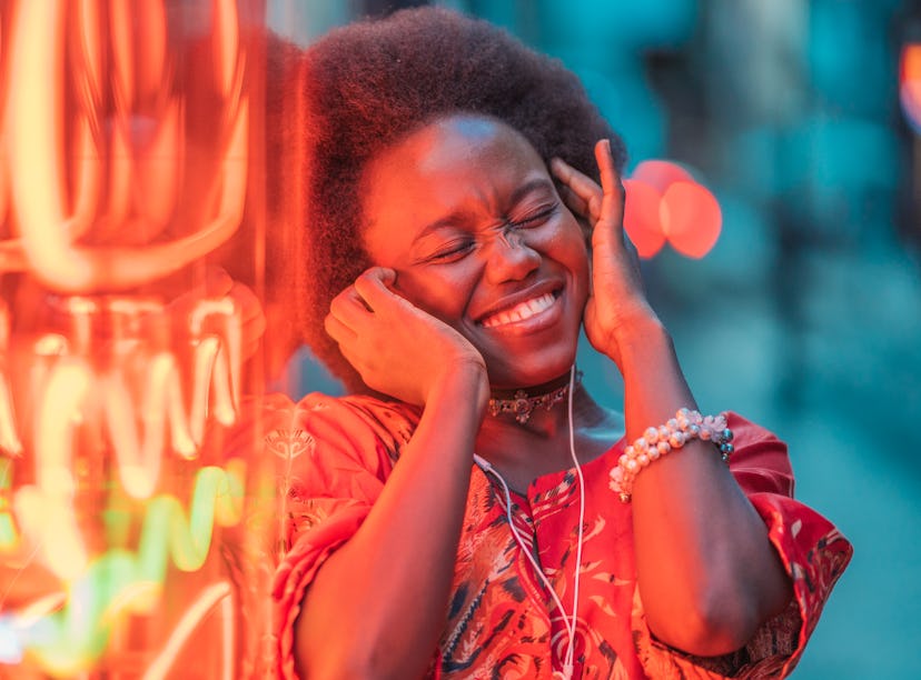 Young woman listening to music next to a neon sign, thinking about how January 3, 2022 will be the b...