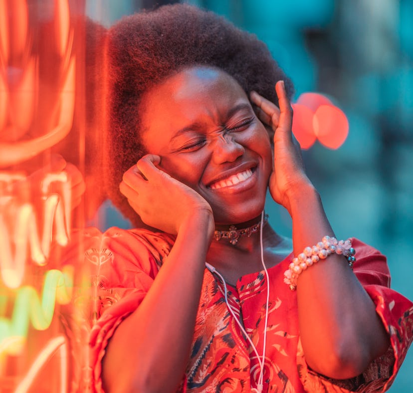 Young woman listening to music next to a neon sign, thinking about how January 3, 2022 will be the b...