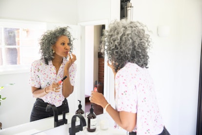 A woman with curly gray puts on makeup in a bathroom