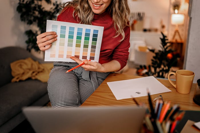 Smiling young woman artist and teacher showing color shade tone chart on laptop while taking worksho...