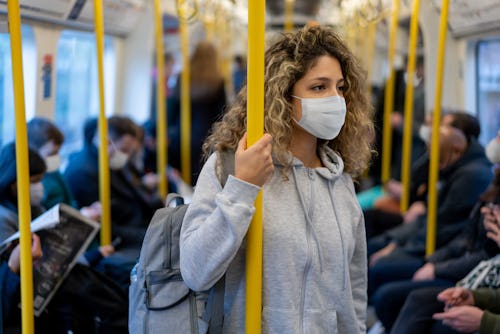 Beautiful young woman riding on the metro wearing a facemask to avoid an infectious disease - COVID-...