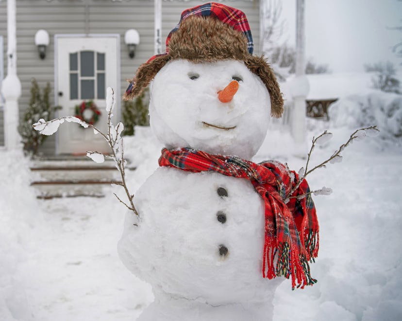 Cute smiling snowman with red scarf and hat in front of a snowy porch on a winter day