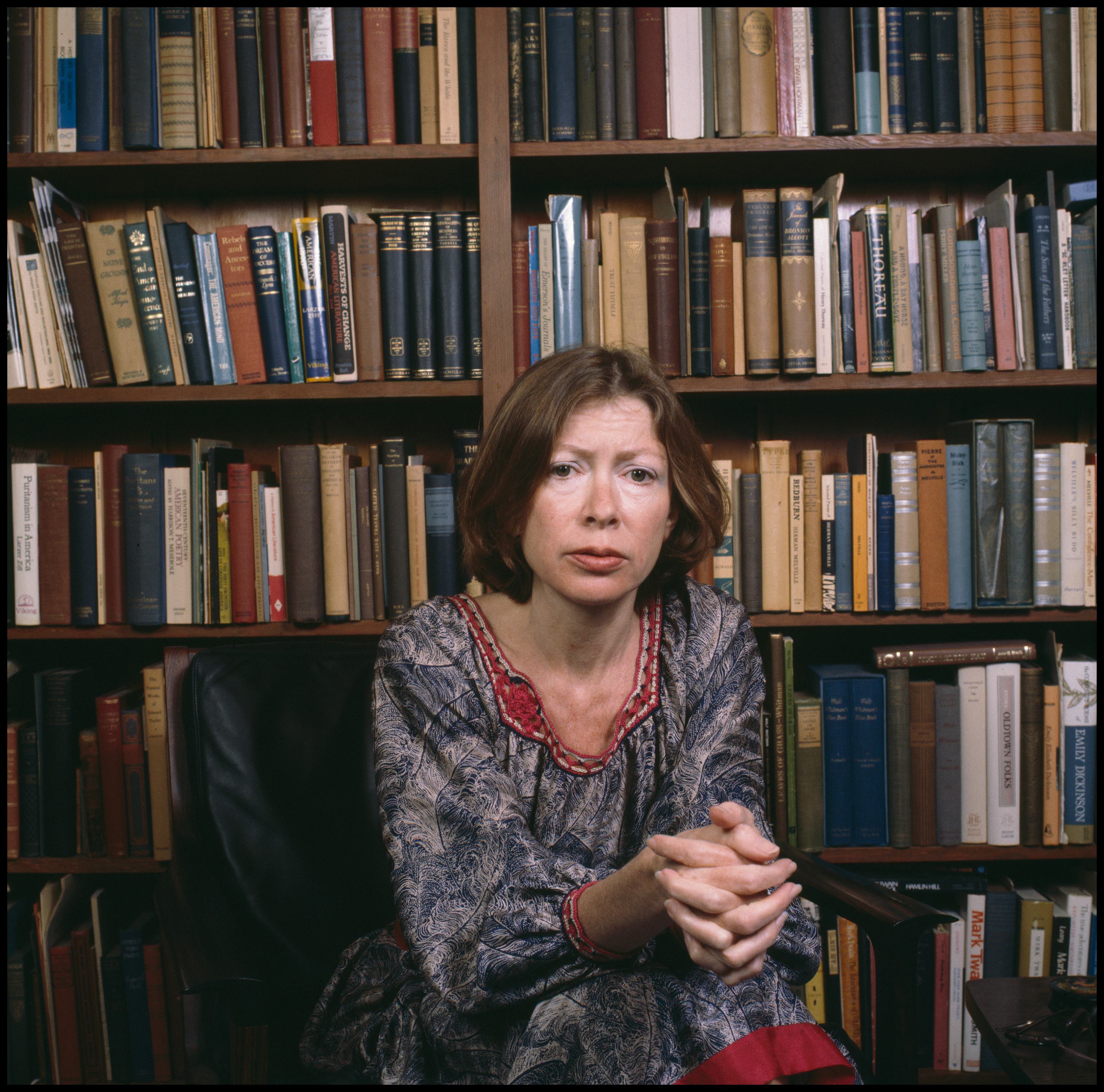 Portrait of American author Joan Didion as she sits in a chair in front of a bookshelf, Berkeley, Ca...