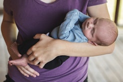 Newborn Caucasian baby boy is sleeping peacefully as mother holds him close to her. Mother is unreco...