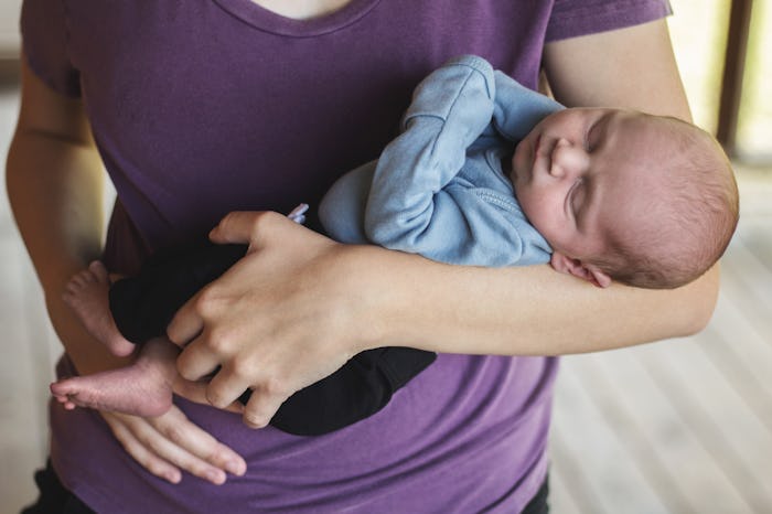 Newborn Caucasian baby boy is sleeping peacefully as mother holds him close to her. Mother is unreco...