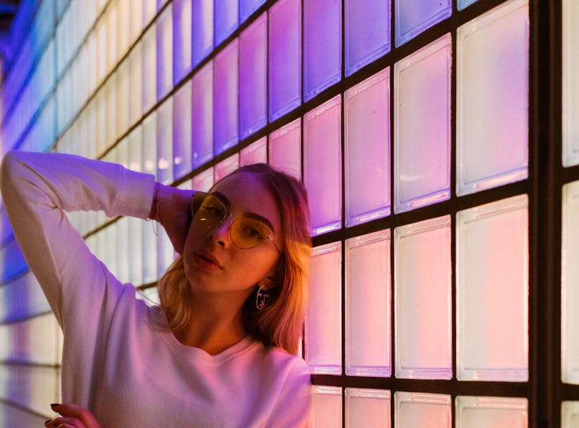 Young woman leaning against a wall of neon lights, thinking about how January 3, 2022 will be the wo...