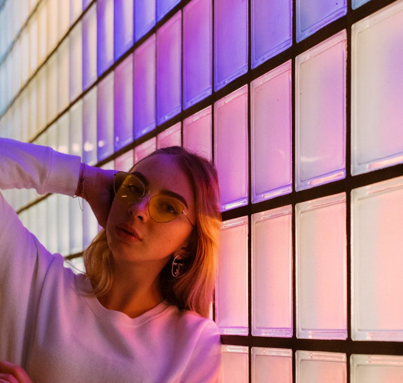 Young woman leaning against a wall of neon lights, thinking about how January 3, 2022 will be the wo...